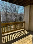 Charming sunlit balcony with wooden railing and scenic view of bare trees, offering a perfect spot for relaxation.