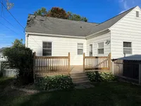 Charming house with a cozy wooden deck, surrounded by lush greenery and a beautifully maintained lawn.