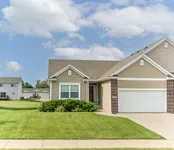 Charming suburban home with a spacious two-car garage, lush green lawn, and inviting entrance under a clear blue sky.
