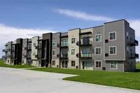 Modern apartment complex with contemporary design featuring spacious balconies, large windows, and a neat green lawn under a clear sky.