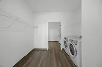 Spacious laundry room with modern washer and dryer, sleek wooden floors, and ample shelving for storage.
