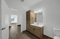 Sleek and modern bathroom with wooden cabinets, elegant lighting, and a view into a sunlit room with stylish wood flooring.