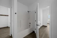Modern bathroom with sleek tub and shower combo, adjacent laundry room with washer, and bright natural light streaming through the windows.