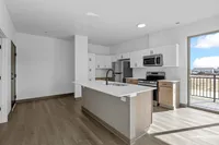 Modern kitchen with sleek white cabinetry, stainless steel appliances, and an elegant island, illuminated by natural light from a large glass door.