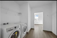 Bright and modern laundry room featuring sleek appliances, airy shelving, and a window with natural light.