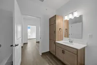 Modern bathroom with sleek cabinetry, large mirror, and hardwood floors leading to a bright room with natural light.