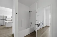 Modern apartment bathroom featuring a pristine bathtub, elegant storage shelves, and a bright laundry room with state-of-the-art washer and dryer.