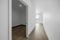 Bright apartment hallway with sleek wooden flooring leading to a sunlit room with expansive outdoor views.