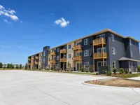 Modern apartment building with sleek exterior design, featuring spacious balconies and surrounded by lush greenery under a clear blue sky.