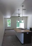 Modern open-concept kitchen and living area with elegant lighting and sleek flooring, featuring a cozy carpeted section with natural light from large windows.