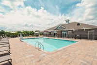 Experience relaxation by the heated outdoor pool, perfect for basking in the sun or enjoying a refreshing swim. Inviting outdoor pool area with sun loungers next to a modern clubhouse under a clear blue sky.