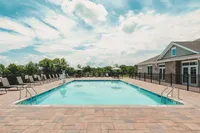 Experience relaxation by the heated outdoor pool, perfect for basking in the sun or enjoying a refreshing swim. Inviting swimming pool with lounge chairs under a bright blue sky, surrounded by lush greenery.