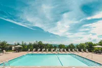 Experience relaxation by the heated outdoor pool, perfect for basking in the sun or enjoying a refreshing swim. Inviting outdoor swimming pool surrounded by lounge chairs and lush greenery under a clear blue sky.