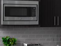 Elegant kitchen featuring sleek GE stainless steel microwave, modern slow close dark wood cabinetry, and stylish subway tile backsplash.