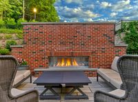 Chic outdoor patio with cozy seating, modern brick fireplace, and lush green surroundings.