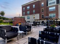 Elegant outdoor patio space with modern seating, cozy fire pit, and ambient lighting against a charming brick building backdrop.