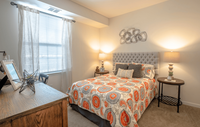 Spacious bedroom in a modern apartment featuring luxury carpeting, ample natural light, and a sleek, contemporary design for a comfortable and stylish retreat. Inviting bedroom with a stylish tufted headboard, colorful patterned bedspread, and warm lighting creating a cozy atmosphere.
