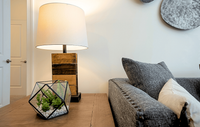 Modern, cozy living spaces with stylish décor, luxury flooring, and warm wood accents for a welcoming feel. Chic living room corner with a cozy couch, stylish wooden lamp, and modern geometric terrarium on a wooden table.