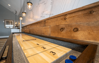 Our clubhouse offers a fun and vibrant space with a billiards table and a variety of games, perfect for relaxing and socializing with friends and neighbors. Chic game room with a stylish wood-finish shuffleboard table, illuminated by elegant hanging lights, perfect for entertainment and relaxation.