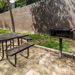 Charming outdoor picnic area with a barbecue grill and rustic table, surrounded by greenery and natural sunlight.