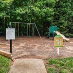 Inviting playground with swings and slides surrounded by lush green trees, perfect for family fun and outdoor activities.