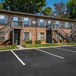Charming brick apartment building with individual entrances, surrounded by lush greenery and spacious parking facilities.