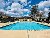 Inviting outdoor swimming pool with sun loungers, surrounded by lush greenery and blue skies, perfect for relaxation.