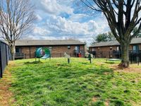 Charming apartment grounds featuring a vibrant grassy area with playful outdoor equipment against a backdrop of cozy brick buildings and a serene blue sky.