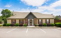 Charming single-story apartment with elegant brick facade, lush landscaping, and welcoming entrance under a bright blue sky.