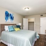Inviting bedroom with elegant decor, featuring a soft blue bedspread, vibrant cushions, modern artwork, and sleek wooden flooring.