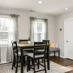 Bright and inviting dining area with a modern wooden table and black chairs, enhanced by natural light streaming through large windows with elegant curtains.