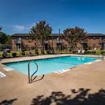 Inviting apartment complex with a refreshing outdoor pool surrounded by lush greenery and elegant lounge chairs.