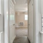 Inviting hallway leading to a bright, cozy room with plush carpeting and modern air conditioning unit.