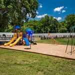 Inviting apartment community with vibrant playground set against lush green surroundings, perfect for families and outdoor fun.
