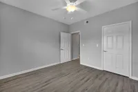 Spacious room with sleek wood flooring and bright, neutral walls, featuring a ceiling fan and double doors, perfect for a serene and versatile living space.