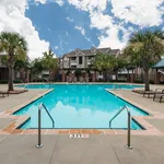 Inviting apartment complex featuring a sparkling swimming pool surrounded by lush palm trees and elegant architecture.