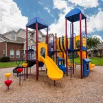 Vibrant playground with colorful slides and climbing structures, set in a lush apartment community.