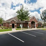 Charming brick apartment complex with lush landscaping and abundant parking, set against a beautiful sky.