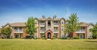 Charming mid-rise apartment building with elegant balconies, surrounded by lush green lawns and trees, perfect for relaxed living.