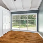 Bright and inviting room with large windows showcasing a lush garden view, complemented by elegant hardwood floors and a vaulted ceiling.