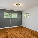 Bright and airy room with elegant hardwood floors, modern light fixture, and large windows offering a view of lush greenery.
