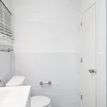Bright and modern bathroom featuring sleek white tiles, a pristine toilet, and stylish window blinds.