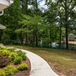 Charming garden pathway leading to serene lake with water fountain amidst lush greenery.