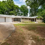 Charming mid-century ranch-style home with a spacious driveway and lush greenery surrounding.