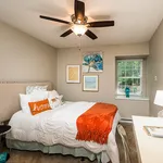 Inviting bedroom with a cozy bed adorned with vibrant orange accents, elegant artwork, and a serene window view.