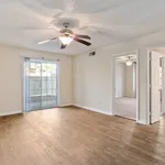 Bright and inviting living area with wooden flooring, modern ceiling fan, and sliding glass doors leading to a private patio.