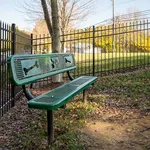 Charming outdoor space featuring a green bench with playful bone and paw designs, surrounded by lush greenery and a secure fence, perfect for pet-friendly relaxation.