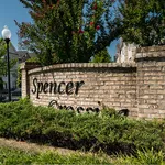 Inviting entrance to Spencer Crossing with lush greenery and brick sign, showcasing a charming community setting.