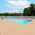 Inviting apartment complex pool with crystal-clear water, surrounded by a spacious deck and lush greenery.