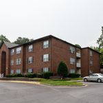 Charming brick apartment building with lush greenery and ample parking, offering a serene residential appeal.